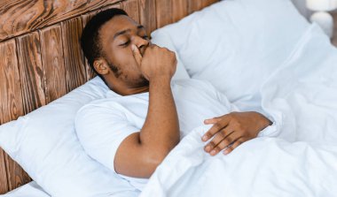 Uykulu siyah adam ağzıyla esneyerek ağzını kapatıyor, evde yatarak uyanıyor. Sabah erken uyanma problemleri, uykusuzluk ve uykusuzluk..