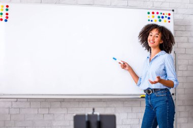 Öğrenciler için online ders. Gülümseyen Afrikalı Amerikalı genç kız tahtayı işaret ediyor ve içerideki webcam 'de İngilizce öğretiyor.