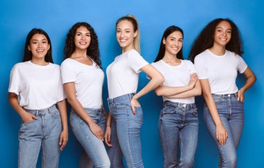 Blue Studio 'nun arka planında kameraya gülümseyen, rahat kot pantolon ve tişört giyen çok kültürlü kızlar. Çeşitli Güzellik Konsepti.