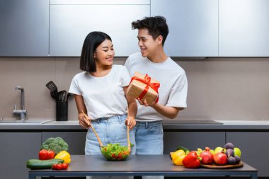 Yıldönümü hediyesi. Asyalı bir çift aile tatilini kutluyor, koca, mutlu karısına hediye paketi veriyor ve modern mutfaktaki yerini şaşırtıyor. Kutlama Yemeği Hazırlama