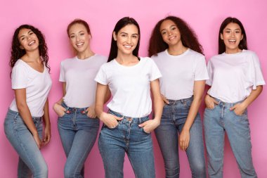 Beş güzel, birbirine karışmış genç bayan stüdyoda pembe arka planda fotoğraf çektirip gülümsüyor ve günlük kıyafetleri ve kot pantolonları giyiyorlar. Mutlu Kadın Grubu, Çok Irklı Güzellik Konsepti