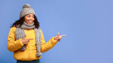 Şuraya bak konsept. Kışlık ceketli siyahi kadın, Mor Arkaplan 'da duran bir şeyin reklamını yapıyor. Kış Reklamı. Stüdyo Çekimi, Metin İçin Boş Alanı Olan Panorama