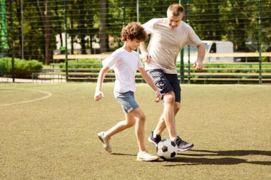 Aktif Yaşam Tarzı. Oğluyla stadyumdaki yeşil çimlerin üzerinde futbol oynayan sporcu bir babanın tam boy portresi.