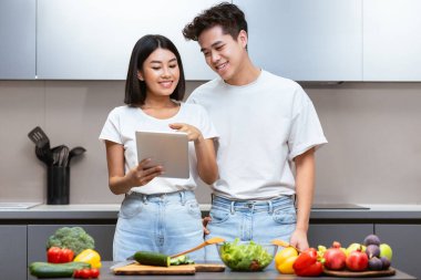 Dijital tabletli Çinli çift internette yemek pişiriyor ve yemek tariflerini arıyor. Evdeki mutfakta birlikte yemek hazırlıyorlar. Sağlıklı Beslenme Uygulaması ve Yemek Uygulaması Konsepti