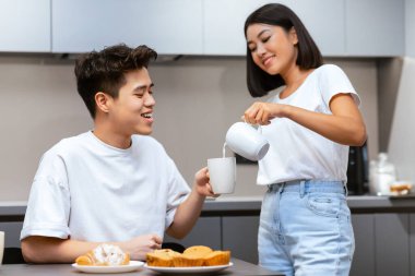 Çinli eş, hafta sonu evde mutfakta aile kahvaltısı yaparken kocasına süt ekliyor. Neşeli Asyalı ev hanımı eşine değer veriyor ve birlikte yemek yiyor..