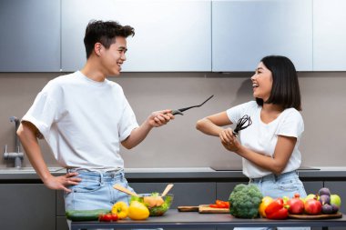 Neşeli Çinli çift mutfakta eskrim yaparken yemek pişirme aletleriyle evde yemek hazırlarken eğleniyor. Kaygısız Asyalı eşler içeride yemek hazırlıklarının keyfini çıkarıyorlar. Beslenme ve Tarifler Konsepti.