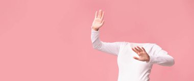 Uzun kollu beyaz gömlekli başsız bir figür yumuşak pembe bir arka plana karşı poz veriyor, neşeli bir hava yayıyor. Kompozisyon vücut dili ve hareketine odaklanıyor, kapris hissi uyandırıyor..