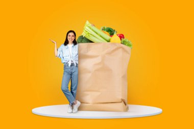 Bir müşteri taze ürünlerle dolu büyük bir kesekağıdının yanında duruyor. Canlı arka plan, bugünlerde market alışverişinin ve teslimatın yeni normalini vurguluyor..