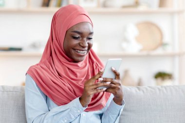 Sosyal ağlar. Genç, tesettürlü, akıllı telefon kullanan, rahat koltukta oturan, arkadaşlarıyla mesajlaşan, internette gezinen, oturma odasında dinlenen, hafta sonunun keyfini çıkaran,