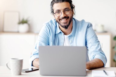 Başarılı bir Freelancer. Milenyum Hindistanlı adam bilgisayarında çalışırken bilgisayarında gülümseyip poz veriyor, göz gözlüğü ve diş teli takıyor ve boş bir alan yaratıyor.