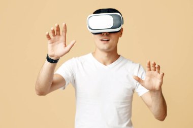 Gelecek, cihazlar, teknoloji, online eğitim, öğrenim. Beyaz tişörtlü ve sanal gerçeklik gözlüklü genç adam ellerini hareket ettiriyor, hareketlerini kontrol ediyor, kumdan arka planda izole edilmiş.