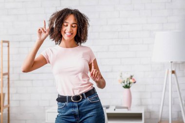 Evde çalışırken en sevdiği müzik. Kulaklıklı mutlu Afro-Amerikan kadın oturma odasında dans ediyor.