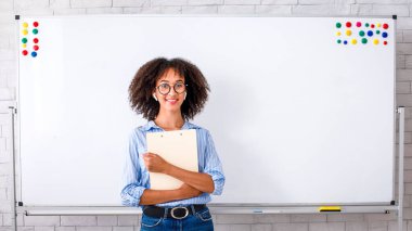 Karantina ve kendini izole etme süresince online çalışma. Beyaz tahta arka planda not defteri tutan, kablosuz kulaklıklı ve gözlüklü tatlı Afrikalı Amerikalı kız.