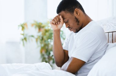 Depresyonda olan Afrika kökenli Amerikalı adam evde, modern yatak odasındaki sorunları düşünerek yatakta oturuyor. Erkek Akıl Sağlığı Konsepti. Metin için Boş Alan