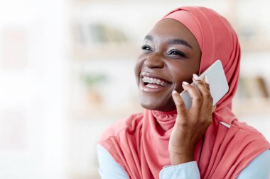 Mobil İletişim. Neşeli siyahi Müslüman kadın cep telefonuyla konuşuyor, başörtüsü ve diş teli takıyor, arkadaşlarıyla keyifli sohbetler ediyor, uzaklara bakıyor, fotokopi uzayı ile yakın plan çekimleri yapıyor.