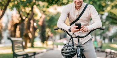 Genç bir adam canlı bir şehir parkında bir anlık eğlencenin tadını çıkarıyor. Akıllı telefonunu kontrol ederken, bisikletinin üzerinde otururken gülümsüyor. Güneş ağaçların arasından süzülüyor, rahatlatıcı atmosferi arttırıyor..