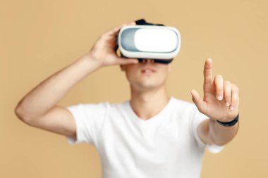 VR gözlüklü bir adam, sanal gerçeklik kulaklığıyla 360 derecelik video izliyor. Beyaz tişörtlü konsantre genç adam boşluğa dokunuyor parmakları kumdan arka planda izole edilmiş, stüdyo çekimi