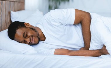 Karnım ağrıyor. Afro-Amerikan bir adam karın ağrısı çekiyor. Karnına dokunuyor. Evde yatakta yatıyor. Sağlık sorunu, karın iltihabı ve mide iltihabı, apandisit konsepti.