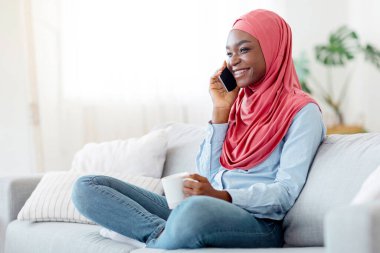 Rahatlatıcı bir hafta sonu. Neşeli, siyah, başörtülü, cep telefonlu bir kadın evde kanepede dinlenirken kahvenin tadını çıkarıyor sıcak çayla rahat bir kanepeye oturuyor, keyifli bir telefon alıyor, Uzay 'ı kopyalıyor.