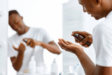 Zenci adam tıraş losyonu kullanıyor. Evdeki banyoda tıraş aynasının yanında durduktan sonra yüz derisi için bakım yapıyor. Erkek Cilt Bakımı Kozmetik Ürünleri, Erkekler İçin Kişisel Bakım Rutini. Seçici Odaklanma