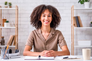 Uzaktan öğrenme dili. Gülümseyen öğretmen masada oturur, kameraya bakar ve öğrencilerle oturma odasında iletişim kurar.