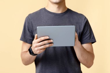 Mobil cihaz ve uygulaması olan serbest çalışan ya da blog yazarı. Akıllı saati olan genç adam dijital tablette yazıyor, bej arka planda izole edilmiş, stüdyo çekimi, boş alan, kırpılmış, panorama