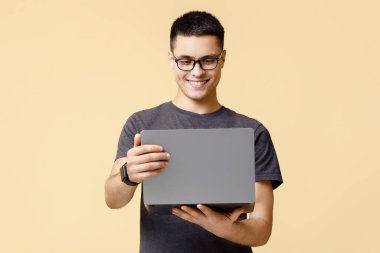 Çevrimiçi eğitim ve iş, sosyal ağlardan gelen mesaj ve iyi bir teklif. Gözlüklü neşeli genç bir öğrenci dizüstü bilgisayara bakar ve konuşur, bej arka planda izole edilmiş, stüdyo çekimi