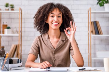 Evde tek başına harika bir iş çıkarmışsın. İş yerindeki Afrikalı Amerikalı kız iyi işaret veriyor ve oturma odasındaki kameraya bakıyor.