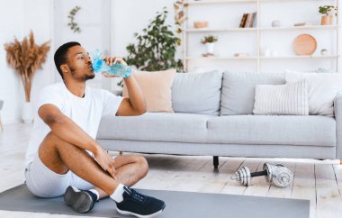 Susuz kalma. Antrenman sırasında su içen, spor salonunda jimnastik yapan siyah adam. Evde eğitim, fitness hidrasyon, spor yaşam tarzı konsepti. Metin için Boş Alan