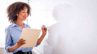 Modern meslek çevrimiçi öğretmendir. Dost canlısı, kablosuz kulaklıklı Amerikalı kız tahtaya İngilizce kurallar yazıyor.