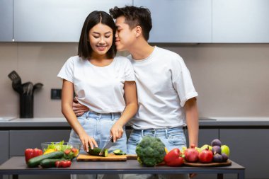 Yemek pişirmenin neşesi. Japon Koca Öpüşen Kadın Birlikte Akşam Yemeği Hazırlıyor Modern Mutfakta Birlikte Bekliyoruz. Salata yapan Asyalı çift. Evlilik Hayatı, Aile Tarifleri ve Beslenme Konsepti.