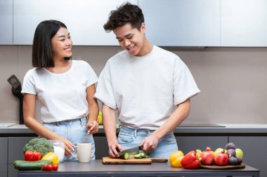 Neşeli Koreli eşler sebze salatası hazırlıyor, birlikte akşam yemeği hazırlıyorlar evde mutfaktalar. Asyalı aile hafta sonları sağlıklı yemek hazırlıklarının tadını çıkarıyor. Beslenme ve Yemek Tarifi