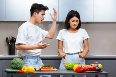 Kızgın Japon koca mutsuz karısına bağırıyor, modern mutfakta yemek pişirirken elini kaldırarak tehdit ediyor. Evlilik Sorunları, Çatışmalar ve Çatışmalar, İlişki Krizi