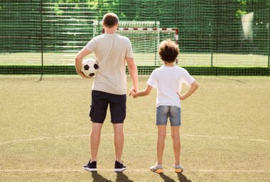 Spor Konsepti. Baba ve oğlunun futbol sahasında el ele tutuşup gol ağlarına baktıkları arka plan.
