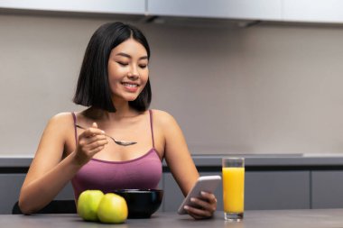 Kilo Verme Uygulaması. Modern mutfaktaki masada oturan ince Koreli kadın kahvaltıda yulaf lapası yiyor. Sağlıklı beslenme, beslenme, zayıflama için diyet. Boş Alan