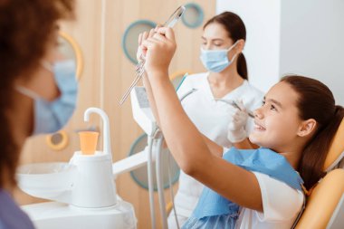 Başarılı diş tedavisi prosedürü, pediatrik diş sağlığı kliniği, modern çocuk ofisi. Mutlu küçük çocuk aynaya bak, dişçi ve hemşire kürklü, koruyucu maskeli ve lastik eldivenli, kesilmiş