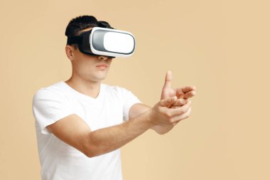 Modern cihazlar ve sanal dünya ile çevrimiçi oyun. VR gözlüklü genç ciddi bir öğrenci hayali tabancadan eliyle ateş ediyor, kumdan izole edilmiş, boş alan, stüdyo çekimi.