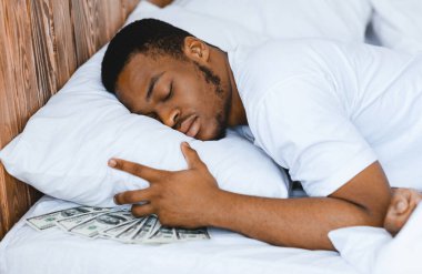 Siyahi adam, yastığın altında para biriktirip evde yatarak uyur. Zenginlik, Mali Güvenlik ve Edebiyat, Banka Hizmetleri Konsepti. Seçici Odaklanma