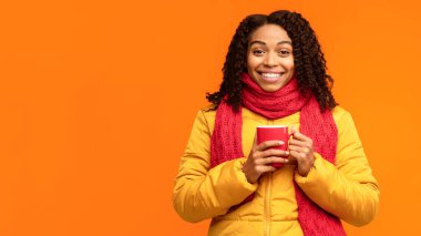 Sıcak Ceketli Afro-Amerikan Kadın Kahve İçme Kupası 'nın tadını çıkarıyor. Sarı Stüdyo Arkaplanındaki Kameraya Gülümsüyor. Kış sezonu, Sonbahar Reklam Bayrağı. Boşluğu Kopyalayan Panorama