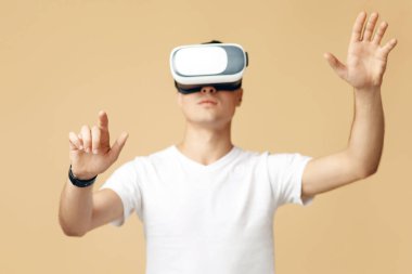 Cihazda oyun uygulaması oynanıyor. Beyaz tişörtlü ve sanal gerçeklik gözlüklü meşgul genç adam jestleri kontrol ediyor, ellere odaklanıyor, kum ya da hafif arka planda izole edilmiş, stüdyo çekimi, serbest alan