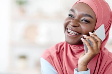 Telefon konuşması. Neşeli siyahi Müslüman kadın cep telefonuyla konuşuyor, biriyle hoş sohbetler ediyor, cep telefonuyla konuşuyor, başka yere bakıyor, diş telleri takıyor, uzay kopyası yapıyor.