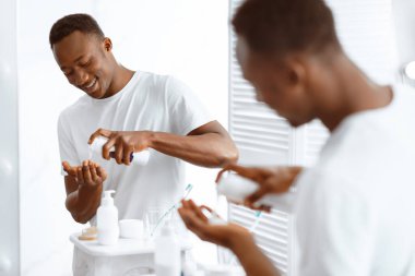 Neşeli Afro-Amerikan Adam tıraş köpüğü kullanıyor evdeki banyoda aynanın yanında duruyor. Erkek Sabahı, Cilt Yüzü Kozmetiği ve Erkekler İçin Kişisel Bakım Programı. Seçici Odaklanma