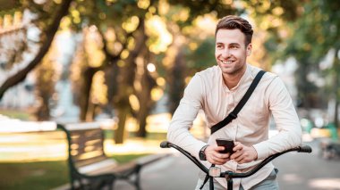Sokak tarzı. Parkta bisikletle otururken telefonla mesajlaşan şık genç adam, boş yer.
