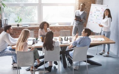 Neşeli uluslararası genç meslektaşlar ofiste iş sunumu yapıyorlar, Asyalı kız ve siyah adam pazarlama raporu hazırlıyorlar