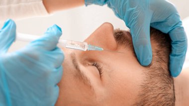 Estetik kliniğinde burun enjeksiyonu yaptıran orta yaşlı bir adamın yakın çekimi. Estetik cerrah yakışıklı sakallı adama yaşlanma önleyici iğne yapıyor. Erkek kozmetolojisi, estetik tıp konsepti