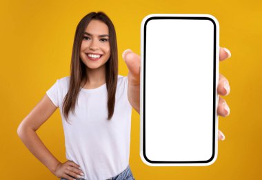 Mobil Uygulama Reklamı. Heyecanlı Kadın Beyaz Akıllı Telefon Ekranı Tavsiye Edici Portakal Stüdyo Arkaplanı Üzerinde Uygulama Pozu Gösteriyor, Kameraya Gülümsüyor. Şuna bak, cep telefonu görüntüsü.