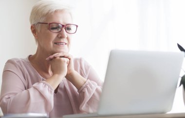 Üst düzey heyecanlı kadın internette makale okuyor, evde dizüstü bilgisayar kullanıyor, boş yer var.