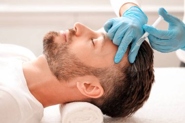 Yakışıklı orta yaşlı bir adamın kuaförde saç bakımını görmesi. Adam estetik kliniğinde mezoterapi görüyor, terapist eldiven takıyor kafa derisine iğne yapıyor, yakın çekim yapıyor.