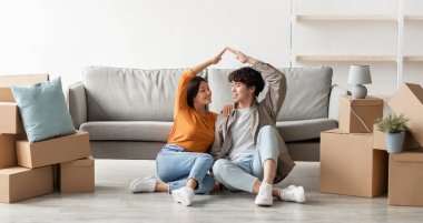 Taşınma günün kutlu olsun. Olumlu genç Asyalı çift kendi evlerine taşınıyorlar, birlikte çatı jestleri yapıyorlar, yerde karton kutuların arasında oturuyorlar, fotokopi çekiyorlar. Panorama