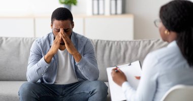 Umutsuz bir siyah adam ruhsal çöküntü ya da depresyondan muzdarip. Psikolog ofisinde, panoramada. Stresli erkek hasta terapistle görüşüyor, profesyonel yardım alıyor.